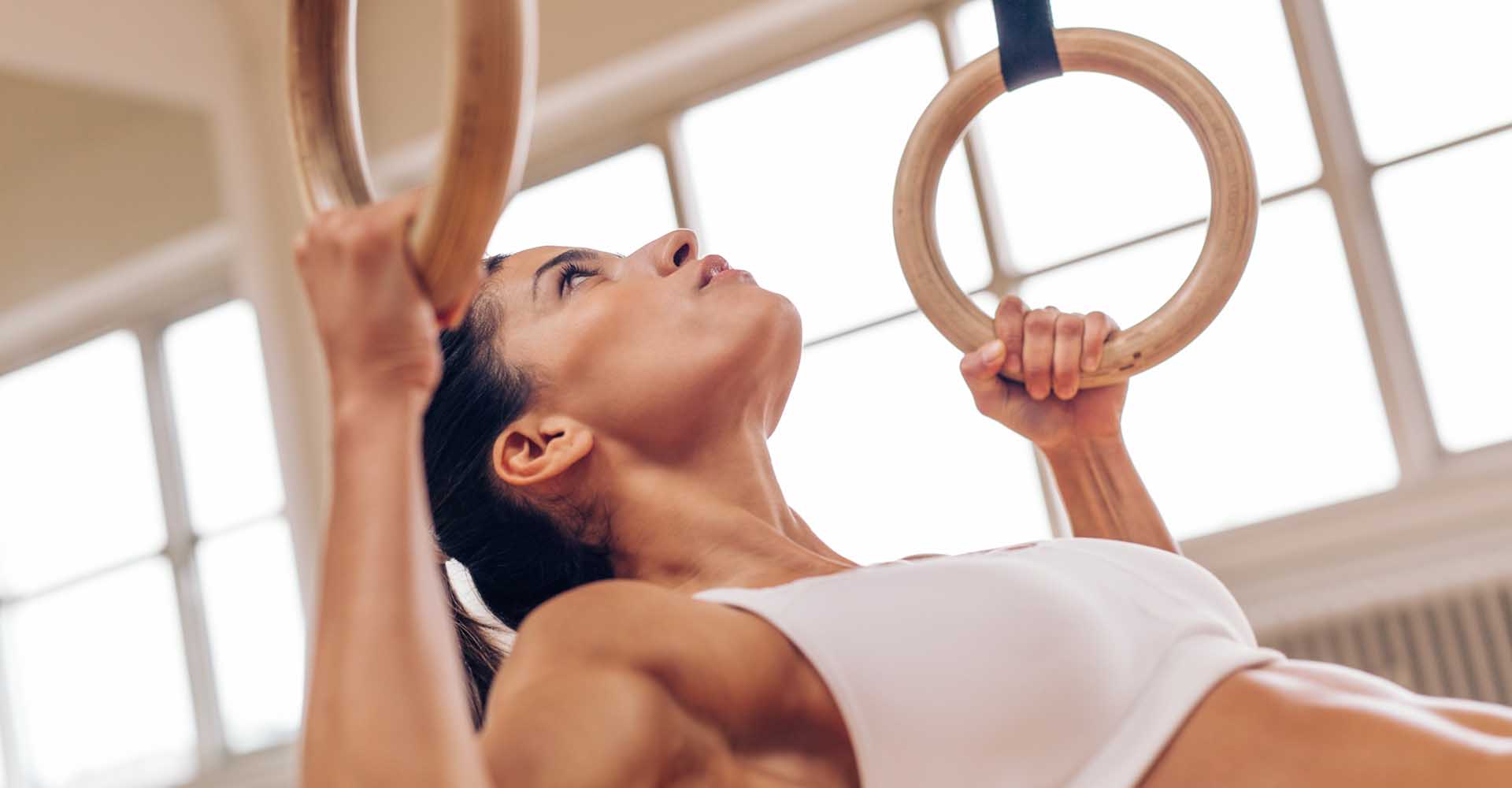 Strong young woman doing pull-ups with gymnastic rings.